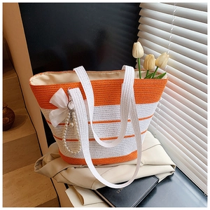 Detalle del bolso de paja con rayas naranjas, lazo de gasa y colgante de perlas