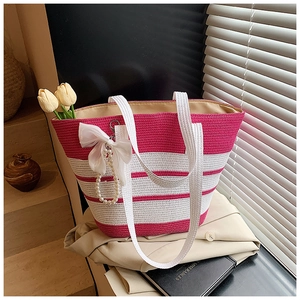 Detalle del bolso tote de paja a rayas con lazo blanco y colgante de perlas de lujo