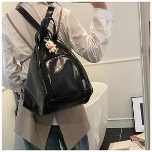 Detail of black glossy backpack with adjustable straps and cute white bear charm
