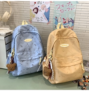 Primer plano de mochilas de lona con diseño de mármol, cremalleras y colgante de oso peluche