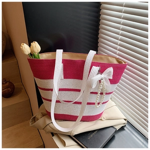 Detalle de bolso de paja con rayas rosas, lazo de seda y colgante de perlas elegante