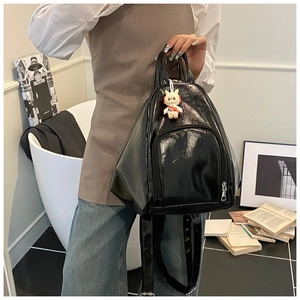 Close-up of shiny black patent leather backpack with a cute white rabbit pendant charm