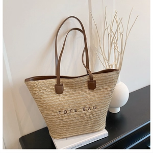 Detail of hand-woven straw tote bag featuring brown leather handles and black embroidery