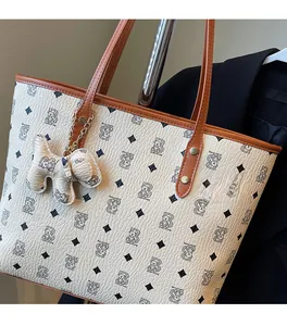 Dettaglio borsa tote color crema con motivo orso, manici marroni e ciondolo a forma di cane