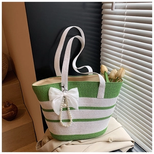 Detalle de bolso de paja a rayas con lazo de seda blanco y colgante de perla elegante