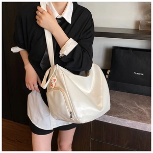 Detail of glossy off-white tote bag with side zipper pocket and cute doll charm