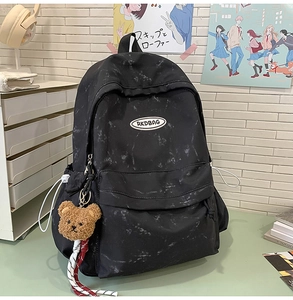 Detalle de mochila negra con patrón de mármol, logo RKDBAG y colgante de osito