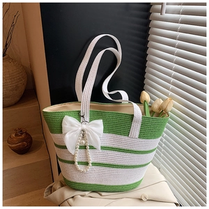 Detalle de bolso de paja de rayas verdes con lazo de seda y colgante de perlas fino