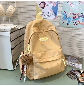Detalle de mochila vintage amarilla con parche de cuero RKDBAG y llavero de osito de peluche
