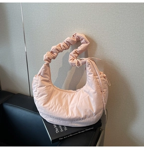 Detail of light pink crescent bag with scrunchie strap on book in minimalist interior