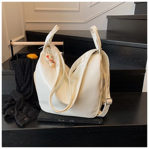 Close-up of minimalist white soft leather tote bag with cute bear charm on black stairs