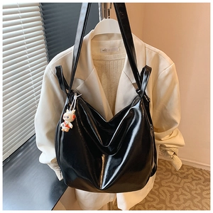 Detail of a large black glossy tote bag with white bunny charm on light suit background