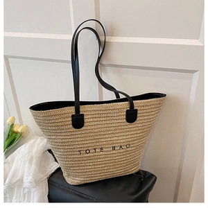 Detail of woven straw tote bag featuring black leather handles and TOTE BAG print