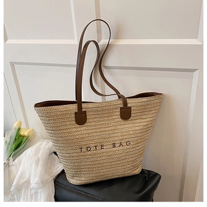 Detail of embroidered TOTE BAG logo on beige straw woven fabric with leather strap