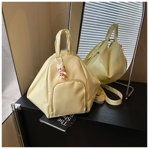 Detail of a cream-colored irregular backpack with a cute rabbit charm and front zip pocket