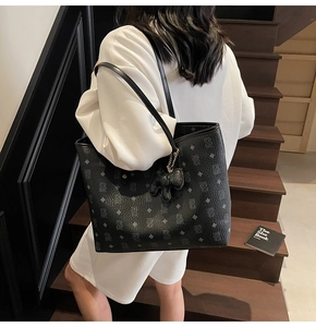 Dettaglio della borsa tote in pelle nera con stampa monogramma e ciondolo a forma di cane