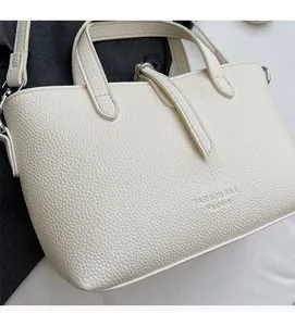 Close-up of pebble-grain cream leather tote showing handle detail and fashion text