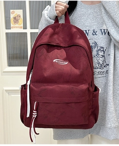 Detail of burgundy backpack showing velvet texture and white braided rope zipper pullers
