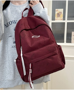 Detail of burgundy canvas backpack with QIJIADYE logo and white zipper pulls shown on model