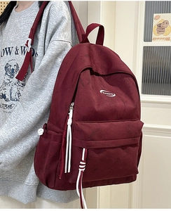 Detail of burgundy canvas backpack featuring zippered pockets and side water bottle holder