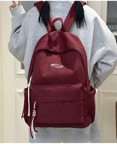 Detail view of burgundy canvas backpack with white logo and zipper tassel on model