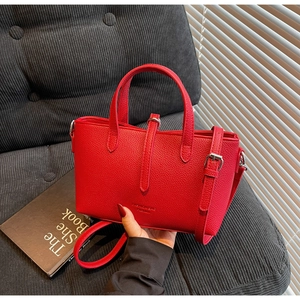 Detail of red lychee grain leather handbag with adjustable strap on a gray sofa