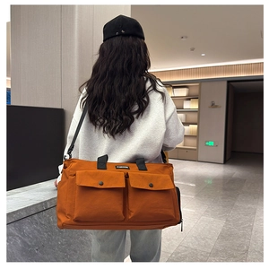 Detail view of large orange canvas travel bag with front pockets and adjustable strap