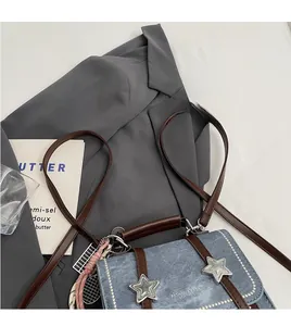 Detail of denim crossbody bag with brown leather trim and silver star buckles