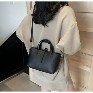 Close-up of black lychee grain leather bucket bag worn by a model with a thin strap
