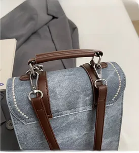Detail of denim patchwork backpack featuring brown leather handle and wavy white stitching