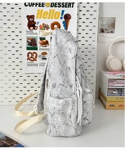 Detail of grey marble pattern backpack featuring white straps on a desk background
