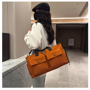 Model showcasing a large orange-brown canvas travel bag with front button pockets