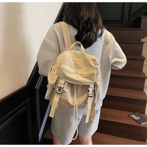 Close-up of beige nylon backpack featuring buckle closures and drawstrings on wood stairs