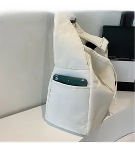 Detailed view of white canvas shoulder bag featuring a functional side pocket for a smartphone