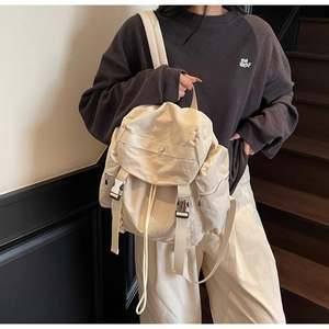 Detail of a cream multifunctional backpack showing flap closure and metal buckle straps
