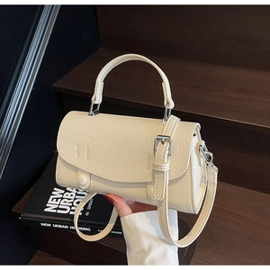 Cream crossbody bag with litchi grain leather on a book and dark wood background