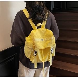Detail of bright yellow wrinkled nylon backpack with silver metal buckles and side pockets
