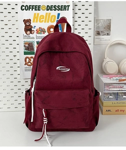 Detailed macro view of burgundy textured backpack with red and white braided zipper pull