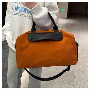 Detail of orange nylon travel bag showing black leather trim and detachable shoulder strap