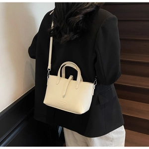 Creamy white pebbled leather bag with double handles shown on a model on wooden stairs