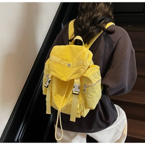 Detail of a bright yellow nylon backpack with silver metal buckles and zippered side pocket