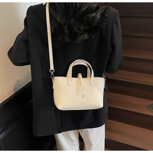 Detailed side view of a cream leather bucket bag with top handles and shoulder strap