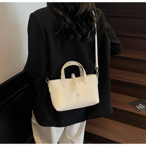 Chic off-white faux leather bucket bag shown as a crossbody on a stylish model