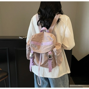 Detail of mauve nylon backpack featuring silver metal buckles and drawstring closure