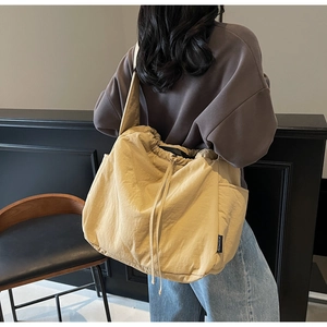 Detail of a large yellow canvas shoulder bag with drawstring closure on a model back