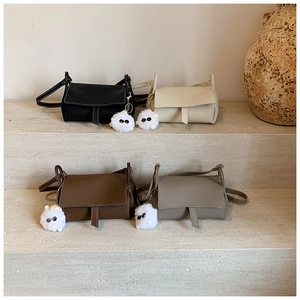 Detailed view of four colorful mini crossbody bags with cute plush charms on stone steps