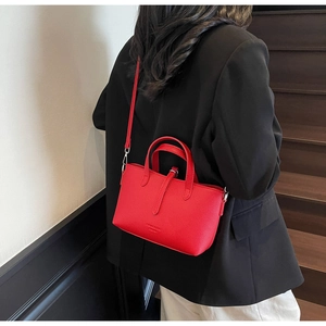 Red lychee textured crossbody bucket bag shown on model with chic black suit styling