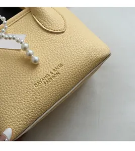 Close-up of creamy yellow lychee leather handbag with pearl chain and logo detail