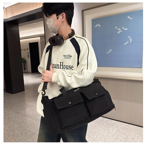 Detail of black large capacity travel bag featuring double front flap pockets and wide strap