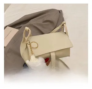 Detailed view of cream leather crossbody bag featuring a soft plush bear charm accessory